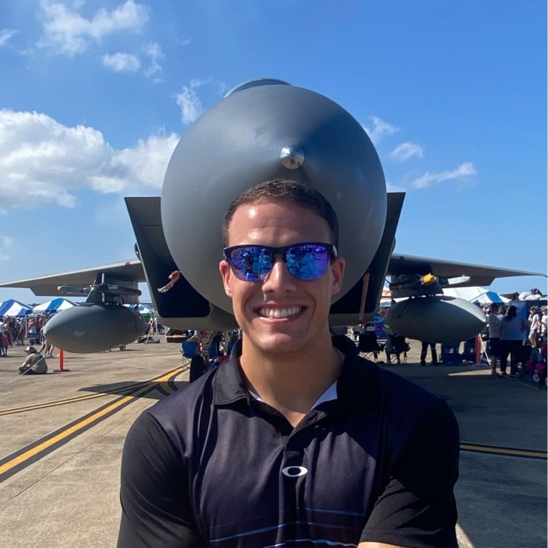 Andrew Oliveri smiling outdoors with greenery in the background